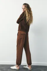 Pantalón jogger color gris claro, de tiro alto con cintura elástica ajustable con cordones, bolsillos delanteros y traseros con solapa, y puños elásticos en el bajo.