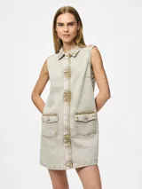 Vestido corto de jean color gris claro, sin mangas, con cuello camisero, cierre frontal con botones y bolsillos delanteros con solapa.