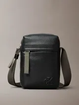 Cartera estilo reportera de Calvin Klein confeccionada en cuero sintético granulado negro. Posee un compartimento principal y un bolsillo frontal con cierre de cremallera, además del monograma de la marca grabado en relieve. Incluye una correa ajustable de color verde oliva.