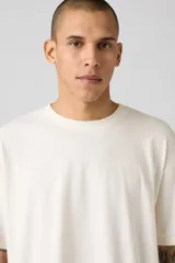 Remera color crema de corte cuadrado y holgado, con cuello redondo y mangas cortas.