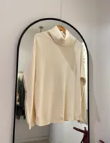 Sweater color crema con cuello envolvente, corte recto y botones decorativos en los laterales. Detalle central tejido en espiga.