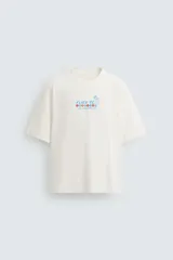 Camiseta color crudo de corte relajado, cuello redondo y manga corta. Estampado frontal con texto "Flies to Los Angeles CA" y diseño de bandera a cuadros.