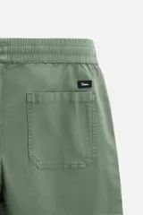 Bermuda color verde militar de corte relajado, confeccionada en tejido de algodón. Tiene cintura elástica ajustable con cordón interior, bolsillos frontales y bolsillo trasero de parche.