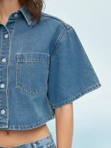Camisa de denim celeste con corte cropped, mangas cortas y bolsillo en el pecho.