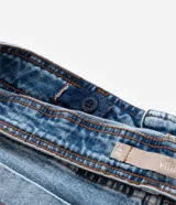 Pantalón de jean azul claro, modelo flare, con cintura elástica, trabillas para cinturón, bolsillos delanteros y traseros, y botón en forma de flor.