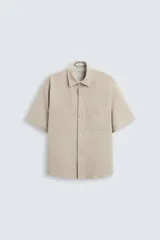 Sobrecamisa color beige de tejido elástico, con cuello solapa, manga corta y dos bolsillos de parche en el pecho. Cierre frontal con botones a presión.