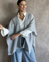 Ruana tejida en lana color gris claro, de corte amplio y diseño abierto.
