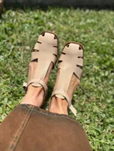 Sandalias nude de cuero con diseño calado y tira con hebilla al tobillo.