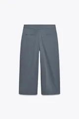 Pantalón marrón de tiro alto, corte ancho y largo midi. Presenta pinzas delanteras, bolsillos laterales y traseros de parche. Cierre frontal con cremallera y gancho metálico.