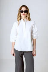 Camisa blanca de corte holgado, cuello mao y mangas largas con puños fruncidos.