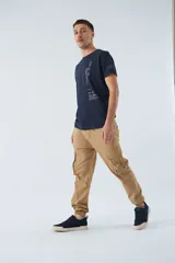 Pantalón cargo color beige, corte slim, con bolsillos laterales con botón, cierre con botón y puños en los tobillos.