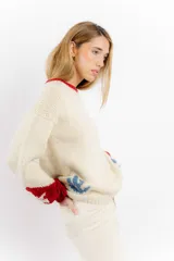 Sweater tejido a mano en lana merino color crudo, con cuello y puños en rojo. Presenta un diseño con motivos de un cowboy y estrellas.