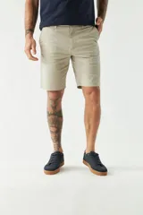 Bermuda color beige, de corte chino clásico, con bolsillos laterales y traseros, cierre con botón y cremallera, presillas para cinturón y logo bordado. Confeccionada en algodón y spandex.