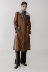 Trench de cuero color camel con cuello de piel sintética color crema, doble botonadura, bolsillos laterales y corte evasé.