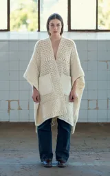 Ruana abierta color crudo, tejida a mano en crochet con lana merino uruguaya. Presenta textura combinada de puntos y trenzas, y bolsillos de cuero vacuno aplicados manualmente.