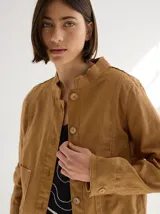 Chaqueta color marrón claro de lino y algodón, con cuello mao, cierre frontal con botones de madera, mangas largas y bolsillos laterales.