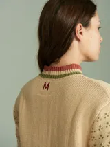 Cardigan de punto color beige con cierre frontal, cuello tortuga y mangas largas holgadas. Presenta diseño con distintas texturas, tejido en ochos a los lados del cierre y apliques de corazones de tela bordados. Confeccionado en 100% algodón.