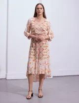 Vestido midi estampado con flores y mandalas en tonos naranja, rojo y celeste, con escote en V, mangas 3/4 con puños fruncidos, cintura elastizada con lazo y ruedo irregular.