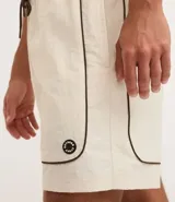 Bermuda deportiva masculina color marrón, con cintura elástica y cordón ajustable. Presenta piping contrastante en blanco a lo largo de los bordes y bolsillos funcionales. Confeccionada en poliamida de secado rápido.