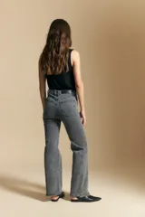 Jean de corte recto y tiro medio, color gris oscuro con efecto lavado. Presenta apliques de tachas metálicas pequeñas en la zona de los bolsillos delanteros.