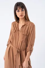 Vestido camisero marrón con cuello clásico, cierre frontal con botones, mangas largas con puños abotonados, cinturón de lazo y aberturas laterales.