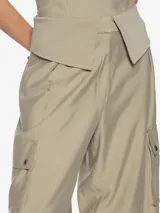 Pantalón color beige, de tiro medio, corte recto y largo hasta las rodillas. Presenta dos solapas que sobresalen de la pretina y dos bolsillos cargo a los costados de las piernas.