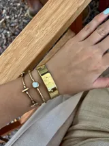 Pulsera rígida dorada con una piedra redonda de nácar en el centro.