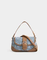Bandolera de denim celeste con estampado floral blanco, detalles en cuero sintético marrón y correa de hombro ajustable. Cierre con hebilla metálica.
