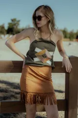 Top strapless negro confeccionado en gamuza con apliques geométricos de cuero en tonos beige y marrón. Presenta flecos en el ruedo.