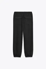 Pantalón jogger color gris claro, de tiro alto con cintura elástica ajustable con cordones, bolsillos delanteros y traseros con solapa, y puños elásticos en el bajo.
