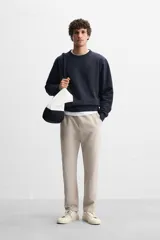 Pantalón de jogging color beige confeccionado en tejido de mezcla de algodón. Cuenta con cintura elástica ajustable con cordón, bolsillos frontales y traseros.