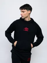 Canguro negro de felpa sin frisa con capucha y logo Umbro bordado en rojo en el pecho. Cuenta con bolsillo tipo canguro y cordones ajustables en la capucha.