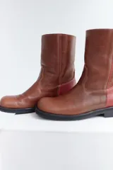 Botas de media caña color marrón de cuero vacuno, con detalle de costuras en la capellada y contrafuerte color bordó. Suela de caucho con taco bajo.