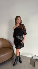 Vestido corto negro de tul con escote asimétrico y mangas cortas. Incluye cinturón negro con hebilla plateada y botas texanas negras.