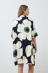 Vestido corto tipo túnica con cuello camisero, manga corta y estampado de margaritas en tonos blanco, verde y azul marino.