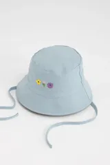 Gorro tipo bucket celeste con bordado de flores en el frente y tiras para atar debajo del mentón.