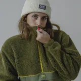 Buzo de polar verde oliva con corte a la altura del pecho en tela lisa color verde militar. Cierre frontal con cremallera amarilla y bolsillo tipo canguro con etiqueta de la marca.