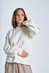 Sweater color crema de hilado frizado con cuello redondo y mangas largas. Presenta apliques de flores en los hombros y mangas.