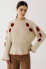 Sweater beige de tejido de punto con apliques de pétalos rojos y detalles dorados.