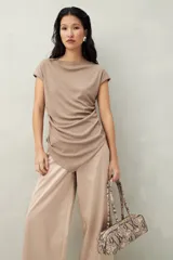 Top color beige de tejido acanalado, con cuello recto, sin mangas y terminación asimétrica en pico.