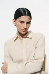 Camisa color crudo de lino liviano, con cuello clásico, botones al frente, canesú de doble capa en la espalda, hombros apenas caídos, mangas largas con puños abotonados, bolsillo superior de parche y bajo levemente redondeado.