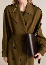 Abrigo largo color verde oliva, de corte oversize, con cuello con solapas, doble botonadura, cinturón desmontable y mangas largas con trabillas.