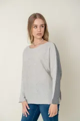 Sweater de lana gris claro con mangas largas y corte holgado. Presenta una franja vertical gris oscuro a lo largo de cada manga.