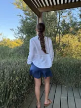 Camisa blanca de lino con cuello mao, mangas largas abullonadas y cierre frontal con botones de nácar. Presenta volados en el frente y puños elásticos.