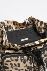 Mochila pequeña con estampado animal print, detalles en negro y múltiples bolsillos externos con cierre.