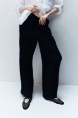 Pantalón negro de corte holgado en tejido de punto con textura. Modelo de tiro alto con cintura elástica y piernas rectas.