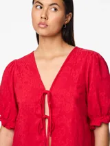 Blusa roja con estampado floral, escote en V con lazos, mangas cortas abullonadas con volantes en los puños y corte cropped.