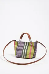 Bolso de mano mini de la marca Bimba y Lola con diseño de rayas verticales en tonos verde, violeta, rosado y blanco. Presenta estructura rígida, asas de mano de piel marrón con herrajes metálicos y una correa larga regulable. Incluye etiqueta frontal con el logo de la marca y cierre magnético.