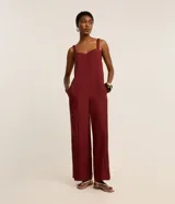 Mono de mujer color rojo oscuro (bordó), de corte recto y pierna ancha, con escote corazón y tirantes anchos con elástico. Presenta pliegues frontales que caen rectos hasta el ruedo.