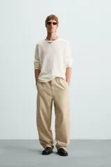 Pantalón de algodón color beige con efecto lavado, corte relajado y pierna ancha. Presenta cintura elástica con ajuste de cordón y cierre frontal con botón, además de bolsillos delanteros y bolsillos traseros de plastrón.